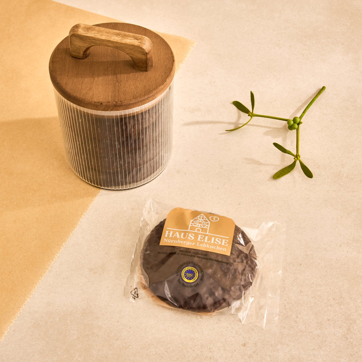 Einzeln in Folie verpackter schokolierter HAUS ELISE Elisen-Lebkuchen mit Etikett, daneben ein Vorratsglas mit Lebkuchen